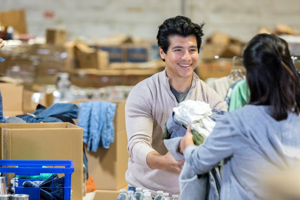 Young male volunteer smiling at a woman as he hands her clothes.